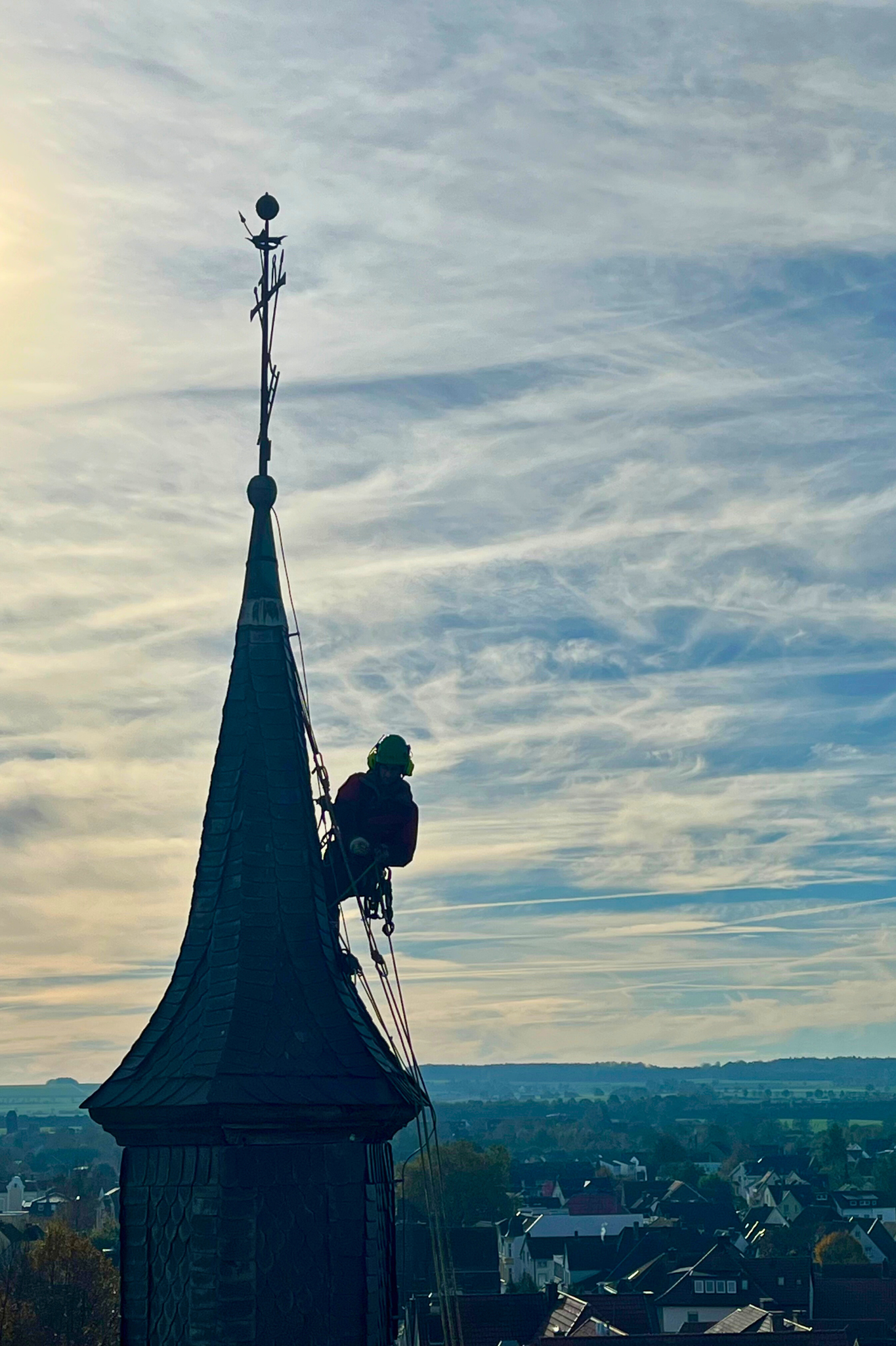 Industriekletterer bei Dachreparatur und Austausch von Schieferplatten an einer Kirchturmspitze